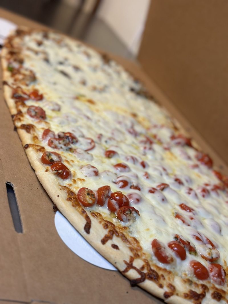 A long pepperoni pizza on a wooden serving paddle