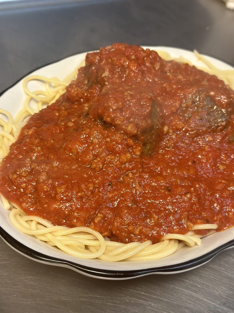 A plate of spaghetti under meat sauce with meatballs, on a stainless kitchen counter