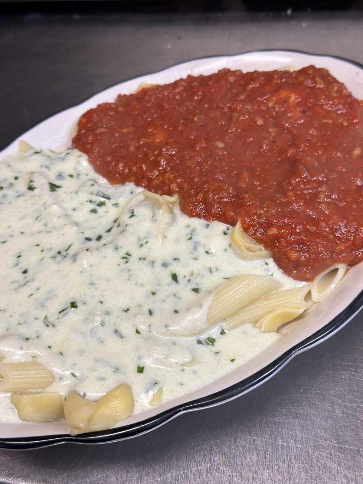 An oval plate of pasta served half with alfredo sauce and half with marinara